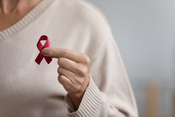 Close up of senior woman hold red ribbon breast cancer symbol support people patient with illness,...