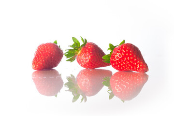 Group of thee ripe strawberries on a white reflective surface. Low level close up shot. 
