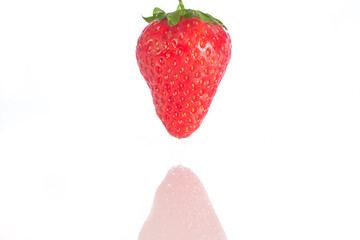 Single isolated strawberry above a white reflective surface.
