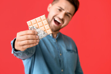 Handsome young man with tasty chocolate on color background