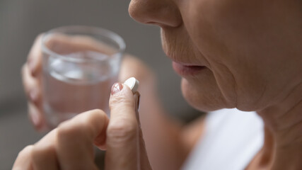 Close up of mature sick woman having antibiotic aspirin pill suffering from headache or migraine, ill senior female take daily dose of vitamin or supplement, medications, elderly healthcare concept - obrazy, fototapety, plakaty