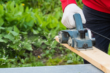 A man's hand holds an electric planing tool . The carpenter does the hardest work.