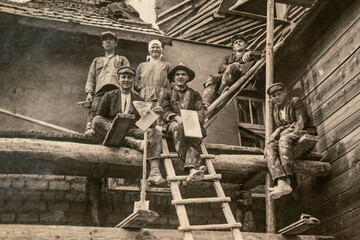 Latvia - CIRCA 1920s: Photo of builders working on site. Sitting on scaffolding. Archive vintage black and white photography - obrazy, fototapety, plakaty