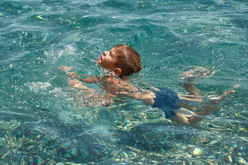 Child boy learning to swim in clear transparent sea.