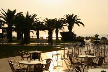 An empty seaside hotel. Street cafe on the background of palm trees at dawn.