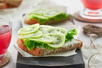 Sandwiches with soft cheese, salad and kiwi on the wooden cutting board. Romantic diet Breakfast for two.