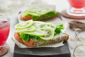Diet healthy Breakfast. Sandwiches with soft cheese, salad and kiwi on the wooden cutting board.