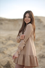 Fototapeta na wymiar Cute young girl model smiles and wears fashion dress. Sand background