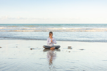 Fototapeta na wymiar Child exercises and meditates on the beach sand