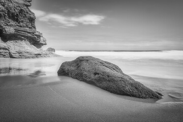 Photo longue exposition de plage avec un rocher au premier plan, noir et blanc.