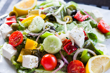 Vegetable salad on the plate, tomatoes, green salad, cheese, lemon and olive, other vegetables.