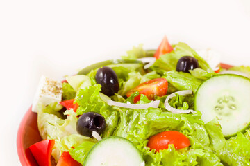 Vegetable salad on the plate, tomatoes, green salad, cheese, lemon and olive, other vegetables.