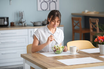 Beautiful young woman eating healthy salad in kitchen