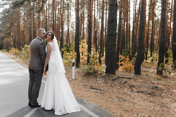 Groom kissing smiling bride while standing in the pines forest. Bride and groom portrait
