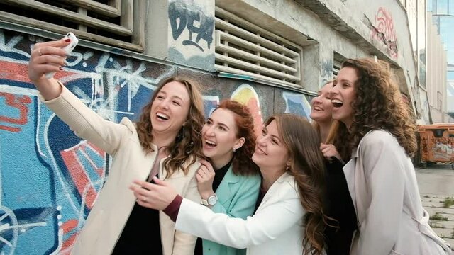 Selfies outdoors in the city. Five girls taking photos on a smartphone against a graffiti background. young people. tourism concept. Happy Summer Fun. 20-25