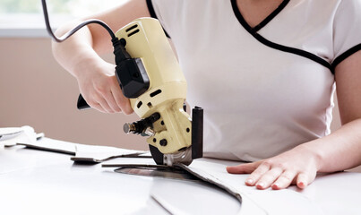 Female worker uses electric cutting fabric machine. Fabric industry production