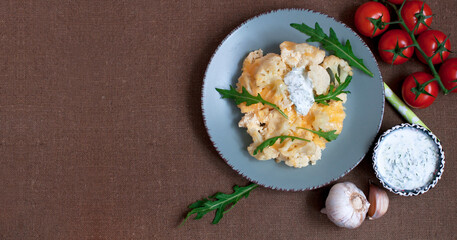 Baked cauliflower and tomatoes with cream-garlic sauce on dark brown background. Top view