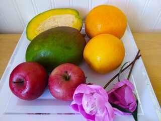 Still life of fruit oranges mango and apples and peony flowers on a white plate