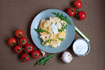 Baked cauliflower and tomatoes with cream-garlic sauce on dark brown background. Top view