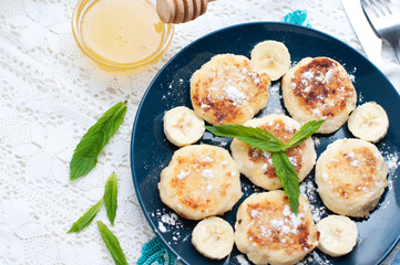 Cottage cheese pancakes, syrniki with banana and mint in blue plate. Breakfast for child. Top view