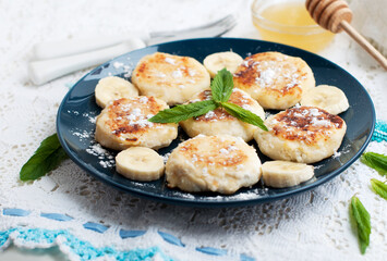 Cottage cheese pancakes, syrniki with banana and mint in blue plate. Breakfast for child