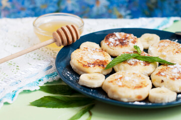Cottage cheese pancakes, syrniki with banana and mint in blue plate. Breakfast for child