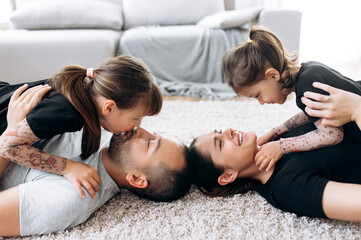 Obraz na płótnie Canvas Happy cheerful family. Family leisure time. Parents spend leisure time with their beloved daughters, they hug and kiss on the floor