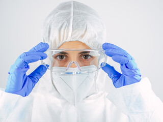 Young woman doctor in uniform, medical cap and mask, close-up portrait. She puts the glasses. Coronavirus concept.