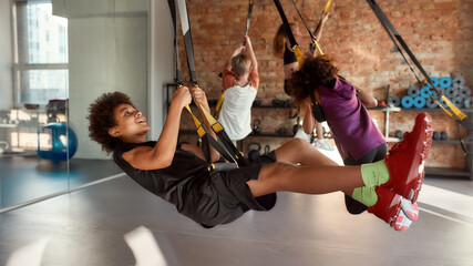 Portrait of teenage boy having fun while training using fitness straps in gym with other kids. Sport, healthy lifestyle, physical education concept