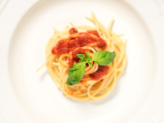 white plate, spaghetti top view, with red tomato sauce and green basil leaves on top