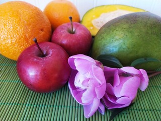 Still life of fruit red apples oranges green cut mango peony flowers on the table