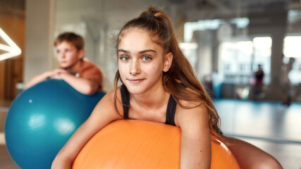 Teenage girl looking at camera while working out using exercise ball in gym. Sport, healthy lifestyle, physical education concept