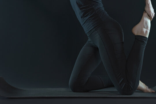 Young woman practicing yoga pose stratching . sport workout fitness. yoga mat and leggins on a dark black background.