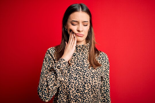 Young beautiful brunette woman wearing casual sweater standing over red background touching mouth with hand with painful expression because of toothache or dental illness on teeth. Dentist
