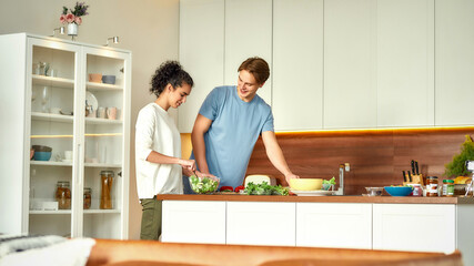 Young man cutting vegetables while woman tossing a salad. Vegetarians preparing healthy meal in the kitchen together. Vegetarianism, healthy food concept