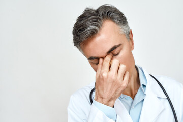 Stress at work. Close up portrait of tired unhappy male doctor feeling upset, keeping eyes closed and touching nose while standing against grey background