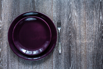 Empty purple plate and a fork on a dark wooden background. Free space for text or logo. Top view.