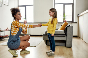 Connected. African american woman baby sitter get acquainted with caucasian cute little girl. They are smiling and talking - obrazy, fototapety, plakaty
