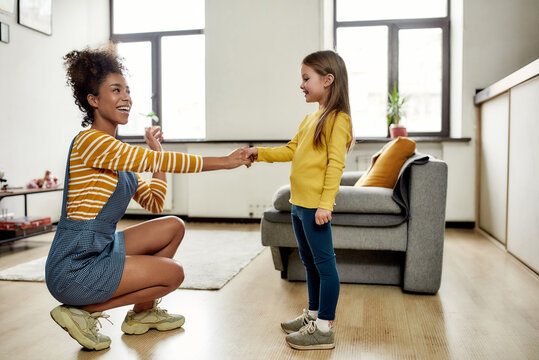 Connected. African american woman baby sitter get acquainted with caucasian cute little girl. They are smiling and talking