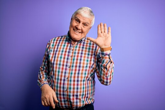 Senior handsome hoary man wearing casual colorful shirt over isolated purple background Waiving saying hello happy and smiling, friendly welcome gesture