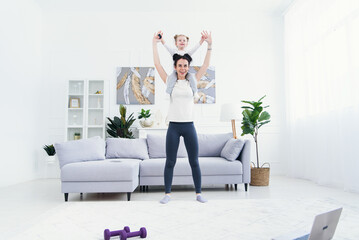 Beautiful mommy and charming little daughter are smiling while doing fitness exercises together at home.
