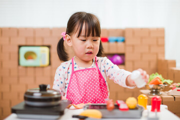 toddler girl pretend play food preparing role against cardboard blocks kitchen background