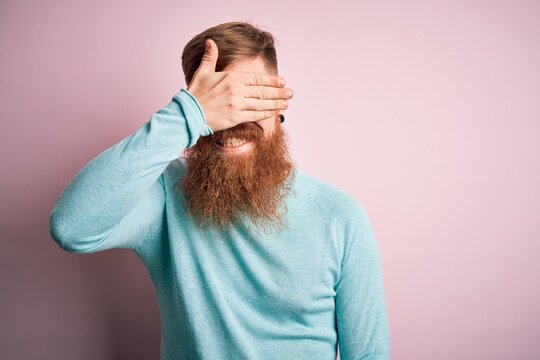 Handsome Irish redhead man with beard wearing glasses over pink isolated background smiling and laughing with hand on face covering eyes for surprise. Blind concept.