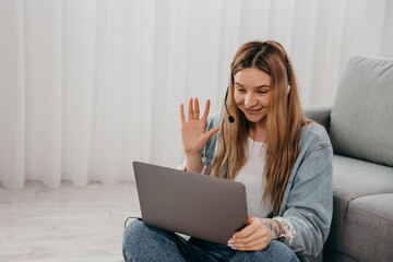 Focused young freelance woman sitting on the table at home with laptop and headphones, working remotely online from home. Concentrated teenage girl studying distantly alone in living room.