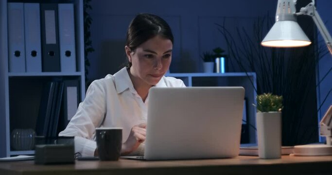 Happy businesswoman working on laptop late night at office