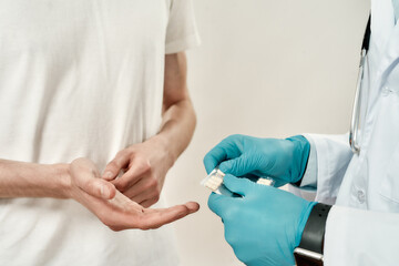 Close up of a doctor in blue sterile gloves giving pills to patient while standing against grey background. Healthcare and medicine. Focus on hands