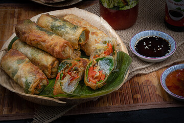Vegan Eggrolls stuffed with bean thread noodles, carrot, peppers and mushrooms on traditional palm leaf plate and banana leaf
