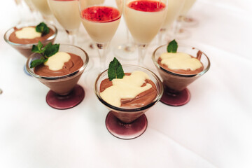 Close up of glasses with sweet vanilla, chocolate or fruit dessert on white table. Self-serving buffet table. Celebration, party, birthday or wedding