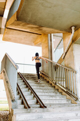 Young fit woman in sport bra running upstairs under a bridge. Fitness outside. Urban run. Cardio.