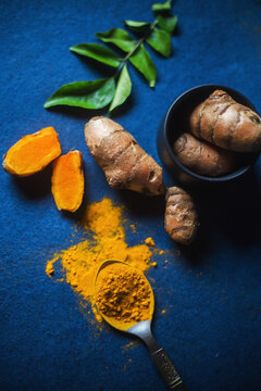 Turmeric Powder and Turmeric Root on a blue background, with curry leaves. Top View of auspicious indian spice haldi.